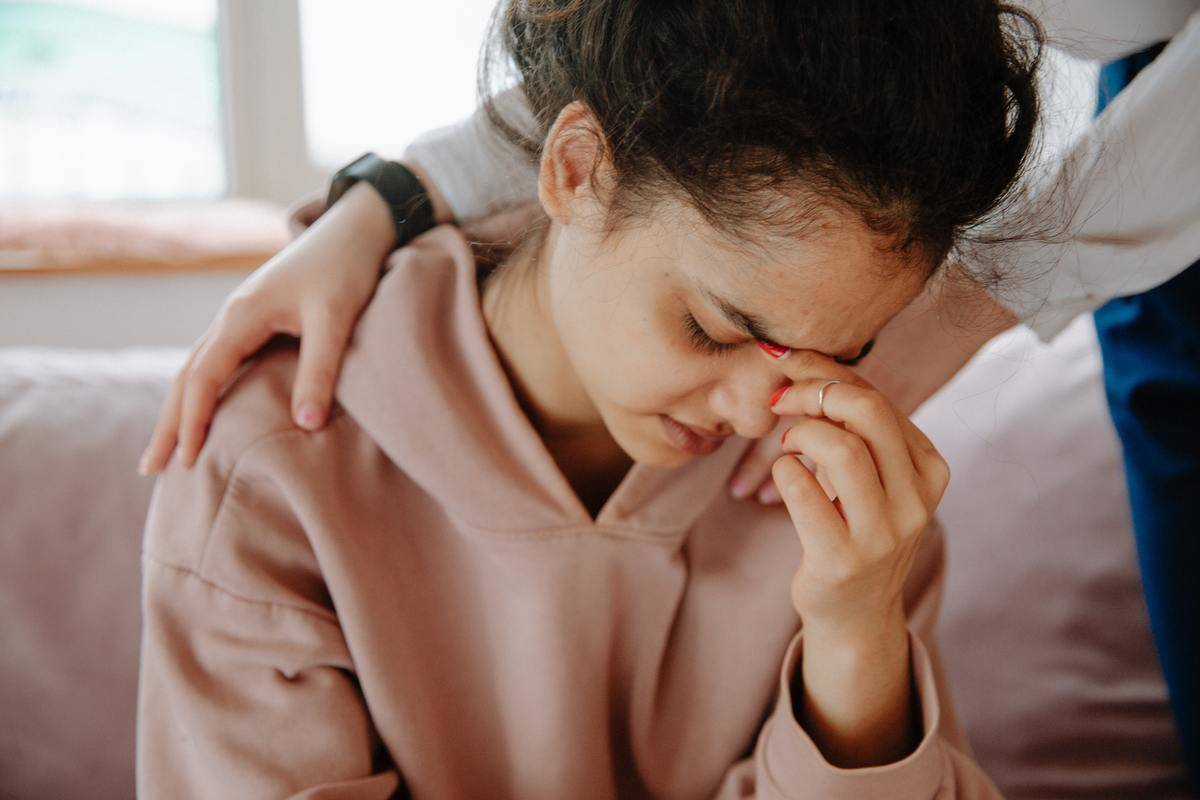 woman in pink sweater looking down, hand pinching nose, upset