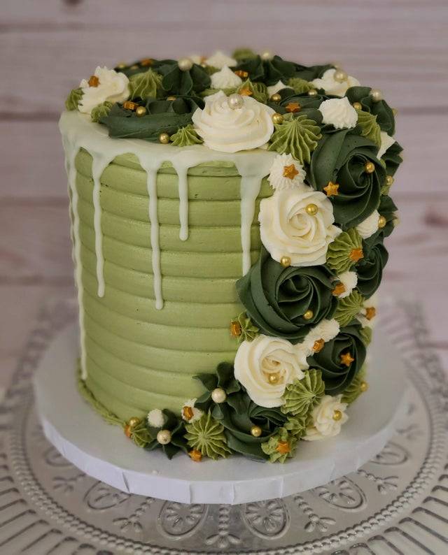cake that's decorated in tones of green and white, frosting flowers, and gold sprinkles