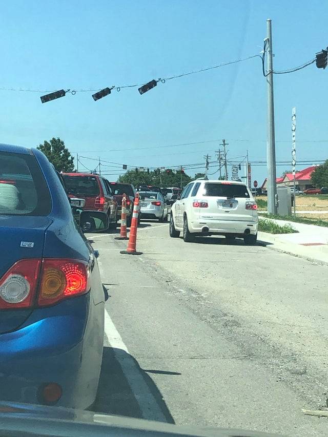 White car on the wrong side of the pylons on the road