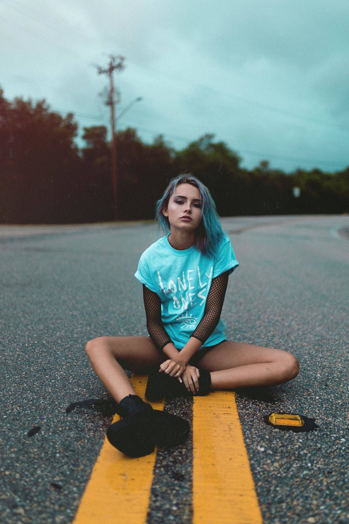 Girl with blue hair sits in the middle of the road 