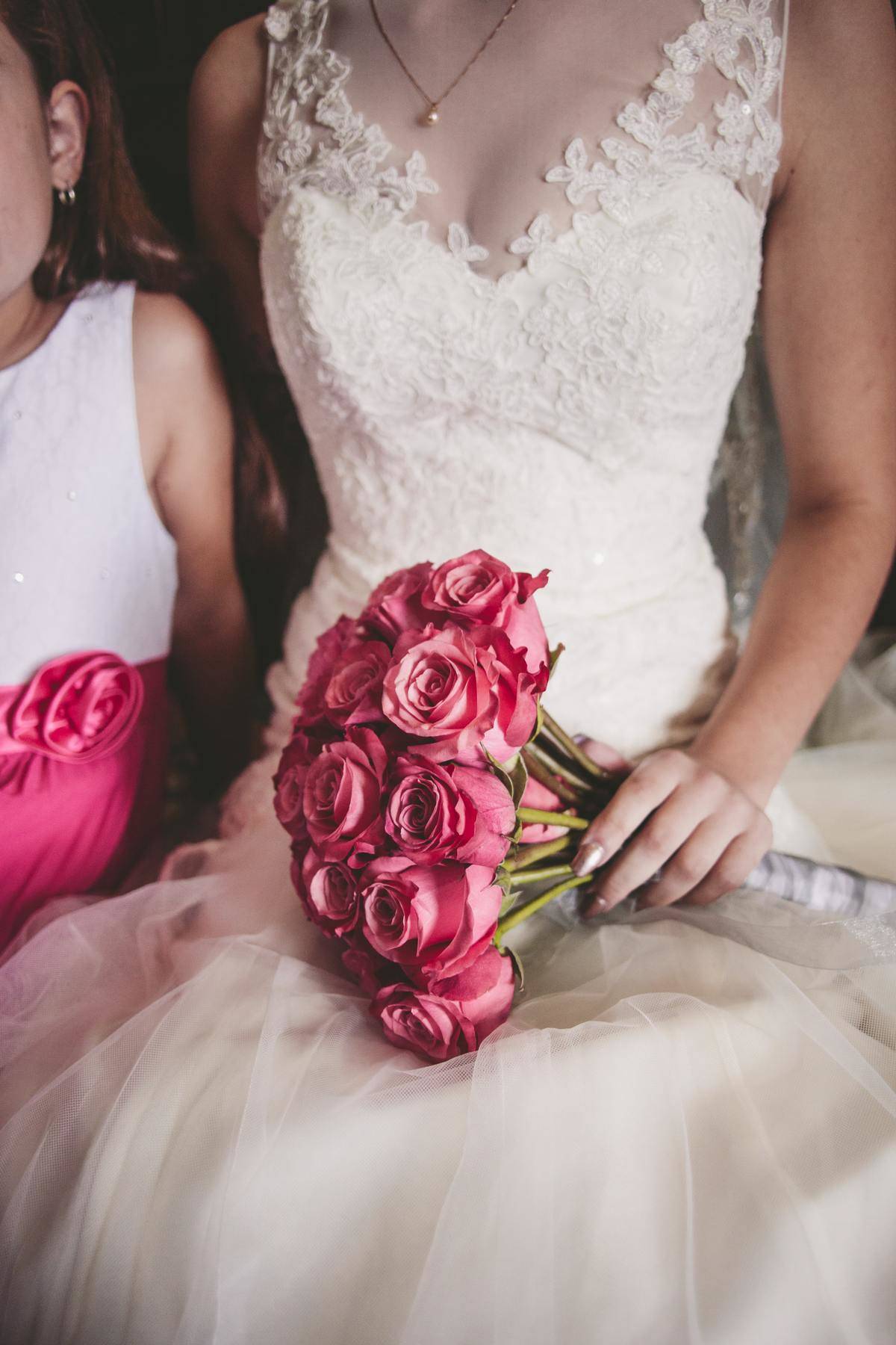 Bride and flower girl sit together while bride holds bouquet of pink flowers 