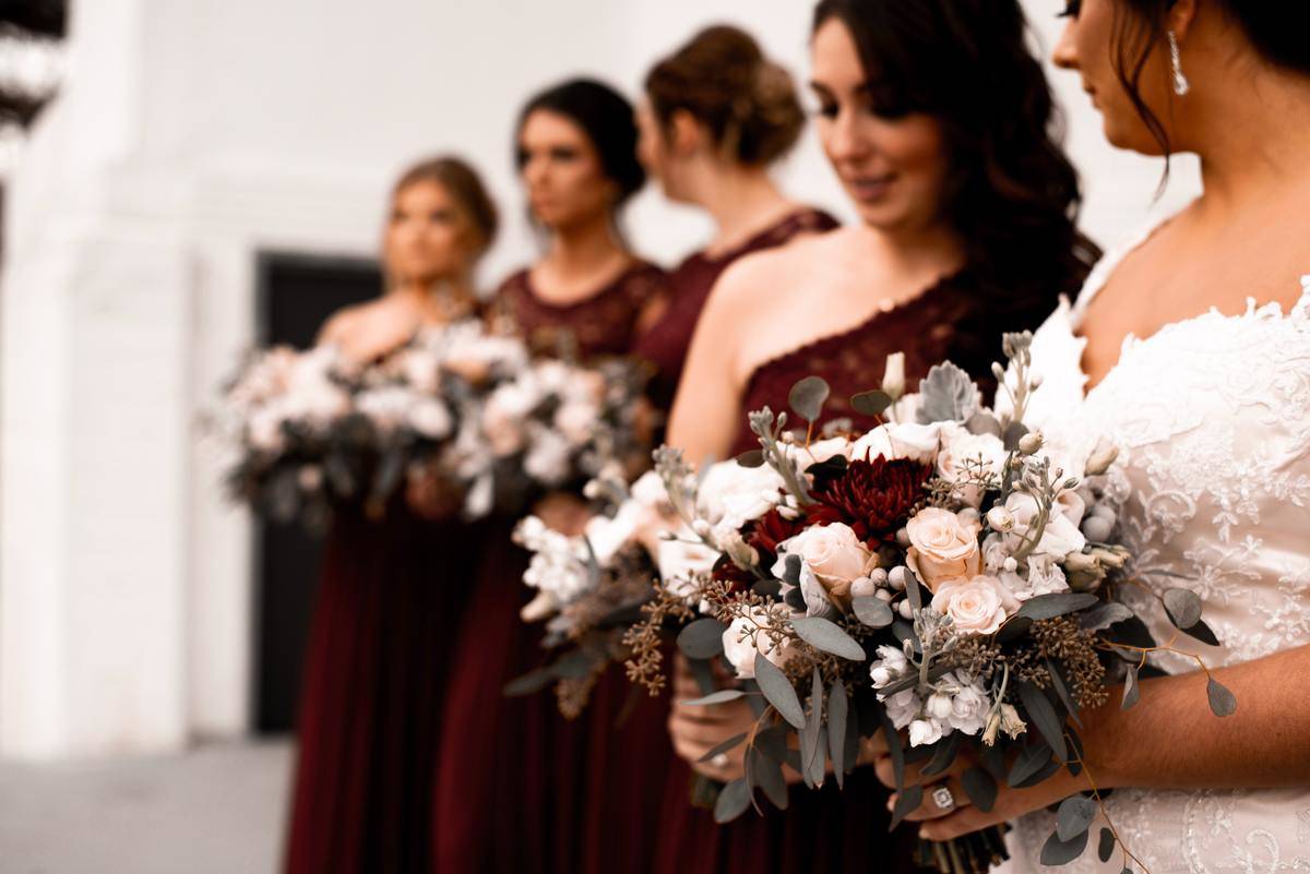 Bride stands with her four bridesmaids who are wearing red dresses and are all holding bouquets