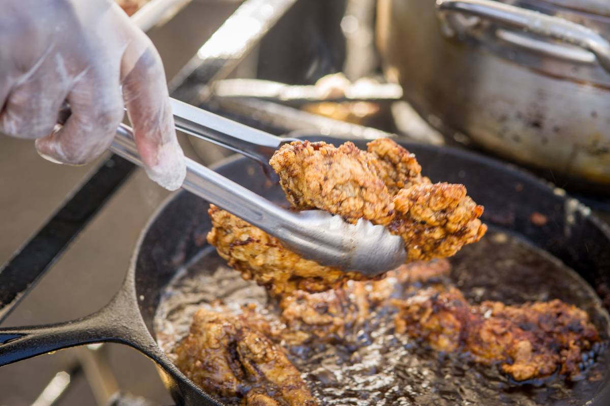 Close-up of tongs pulling out fried chicken from a cast iron pan