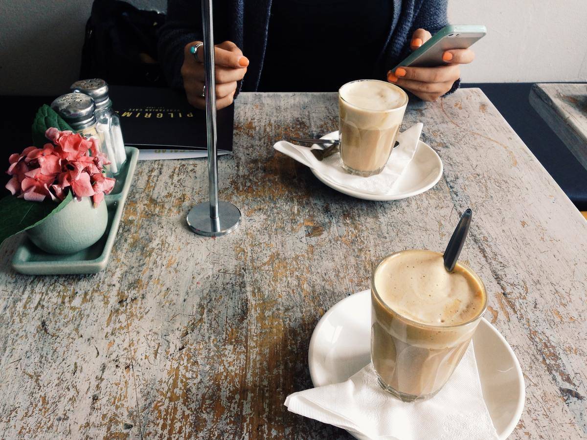 Woman holding phone while sitting across from someone, each with a coffee in front of them on the table