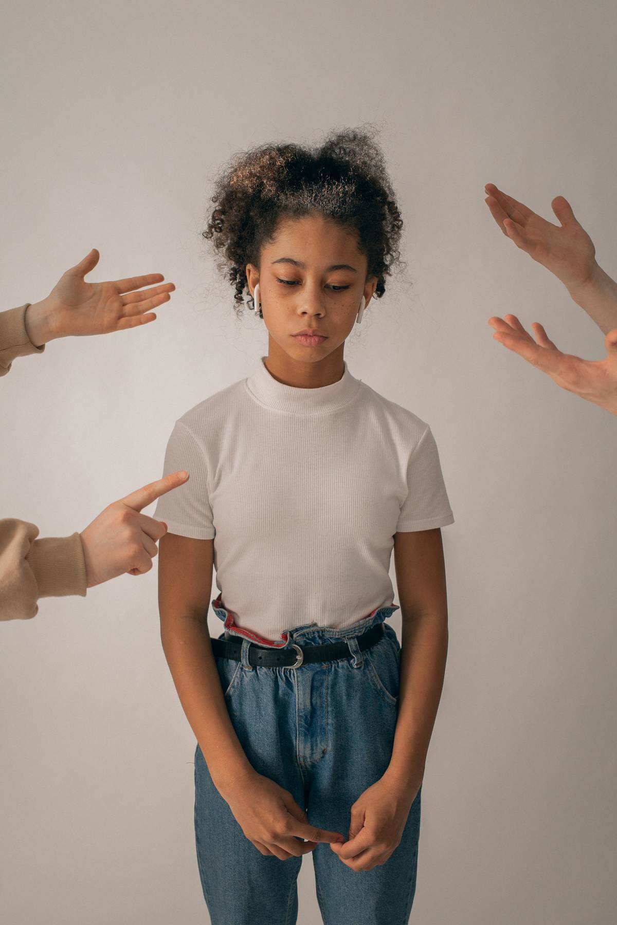 Young girl stands by herself looking upset with many hands wagging their fingers at her