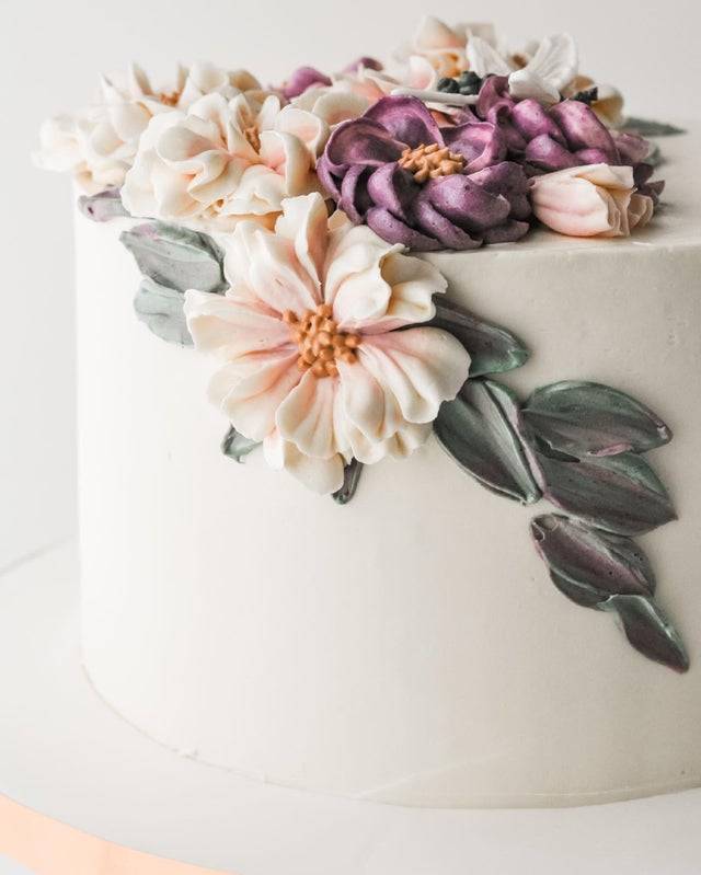 A white cake with hand-piped buttercream flowers and greenery