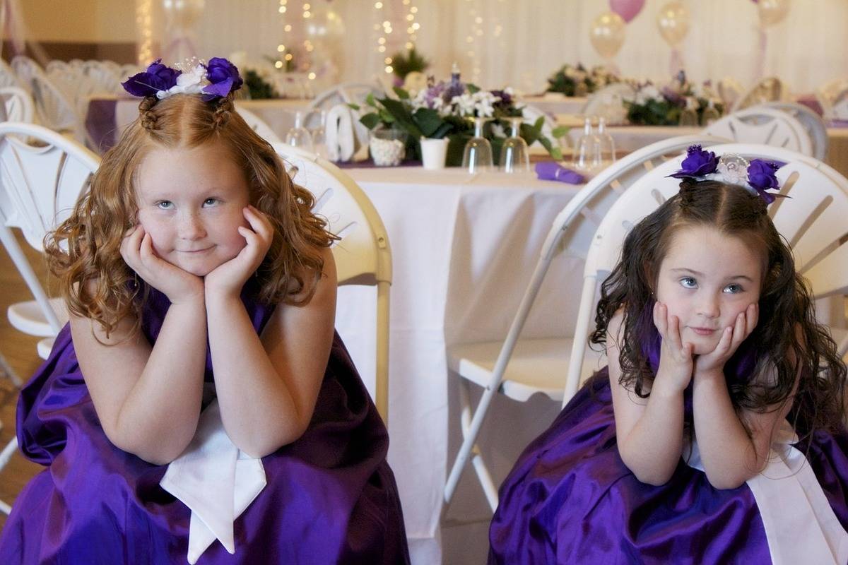 Two flower girls in purple seating inside a hall for a wedding reception