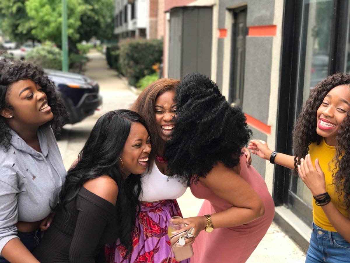 Group of five women laugh and hug on street