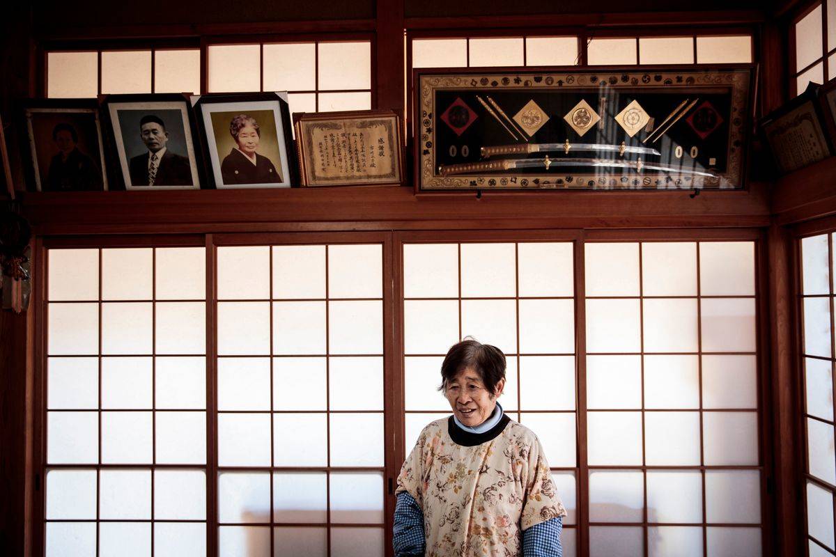 Elderly Japanese woman Taeko Miyazaki poses under family pictures in her house in Kagamimachi