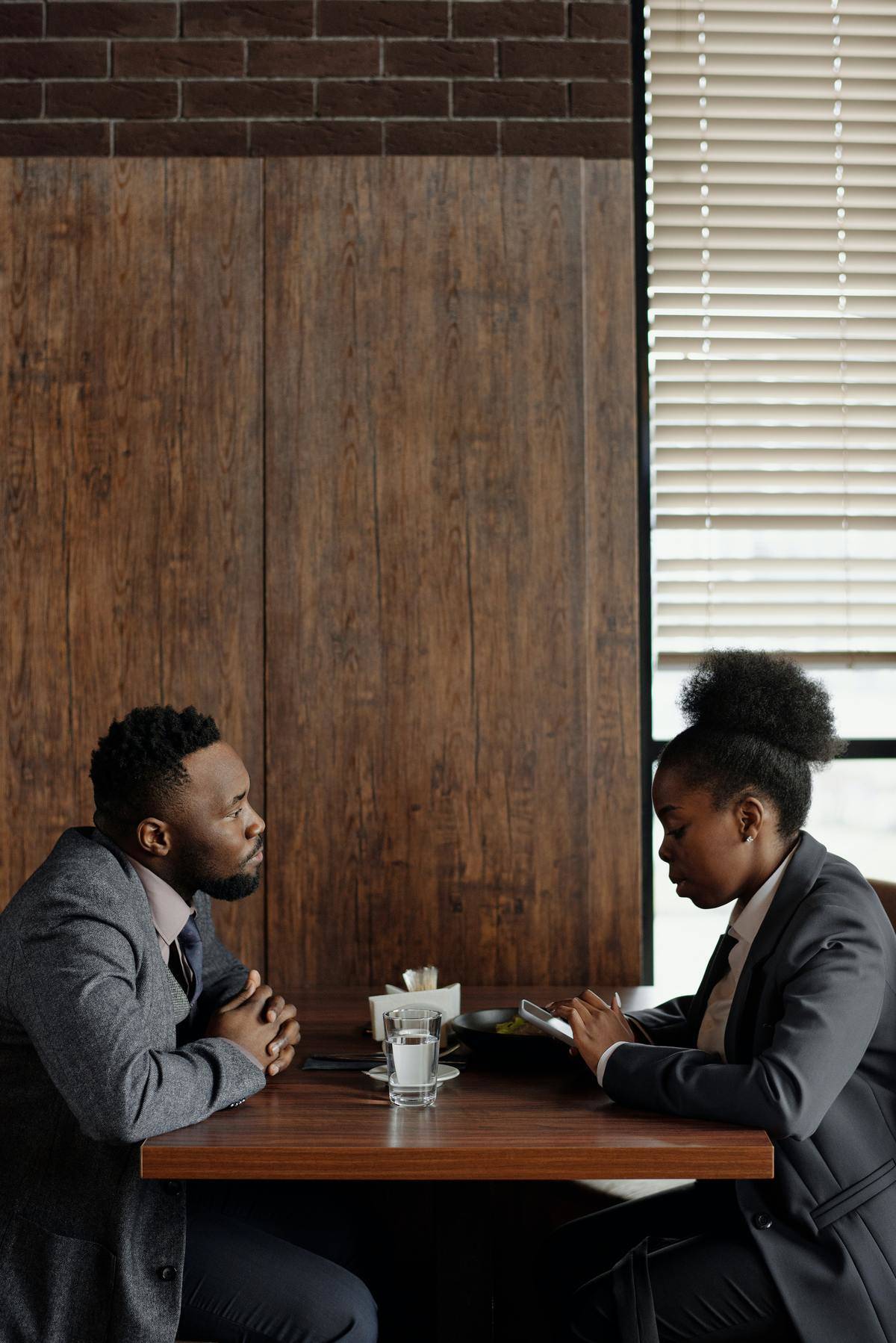 Woman looking down at her phone while seated across the table from a man who is looking at her
