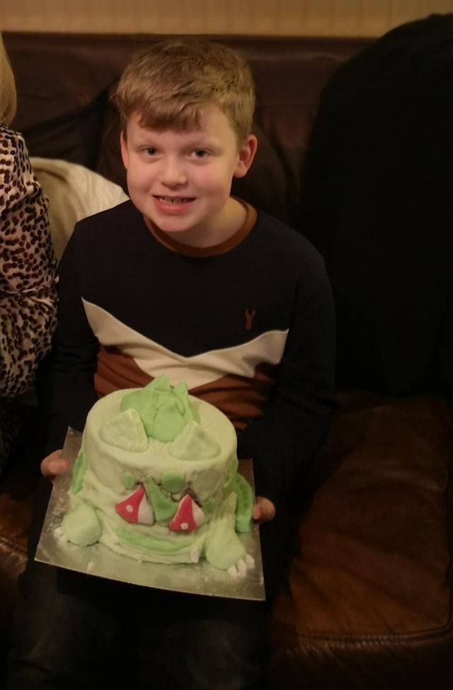 A boy holds his wonky green birthday cake
