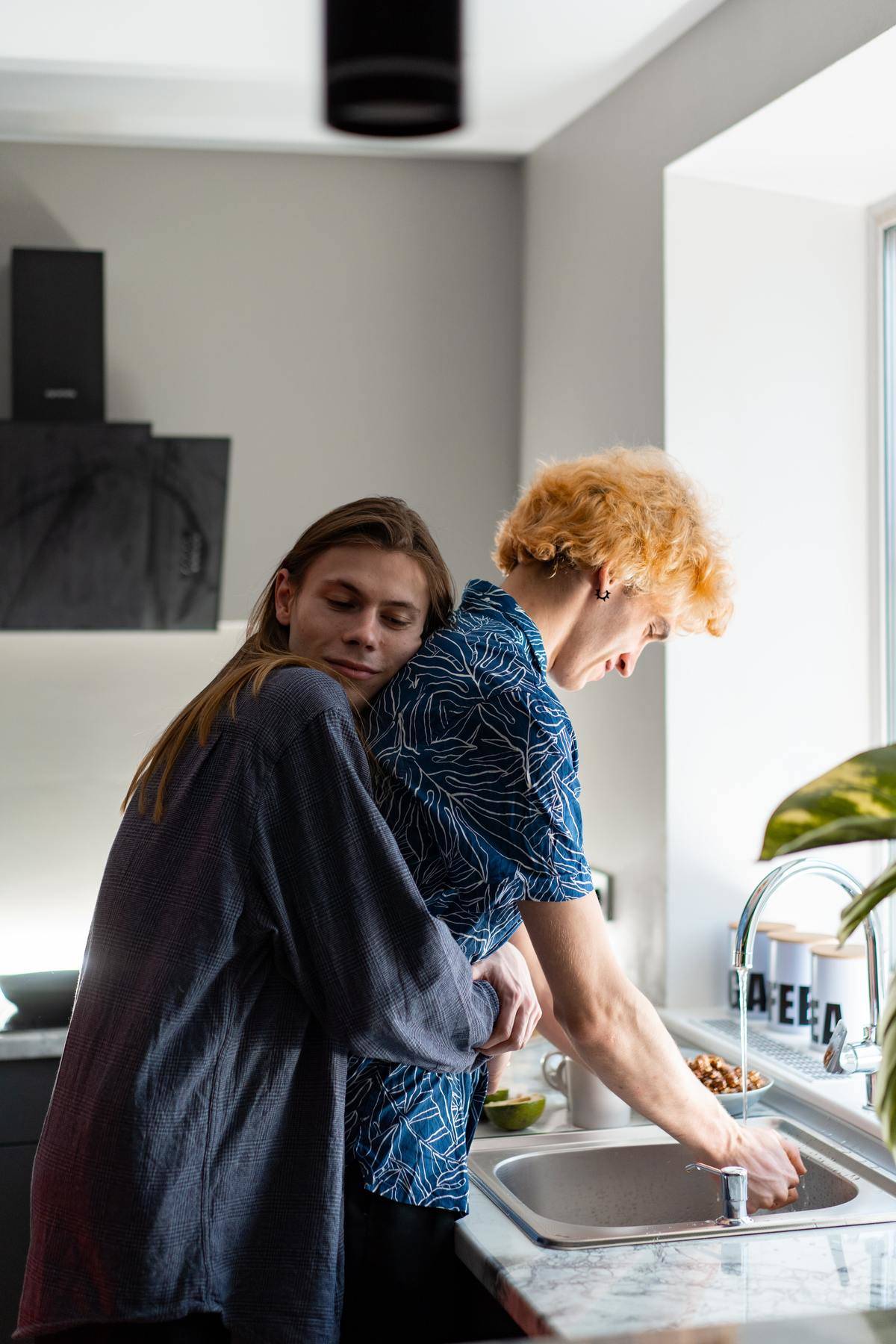 Man is doing dishes while woman hugs him from behind