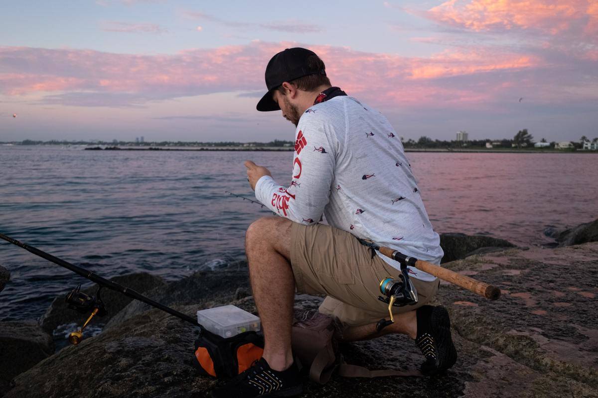 Man ties lures on his fishing line at sunset