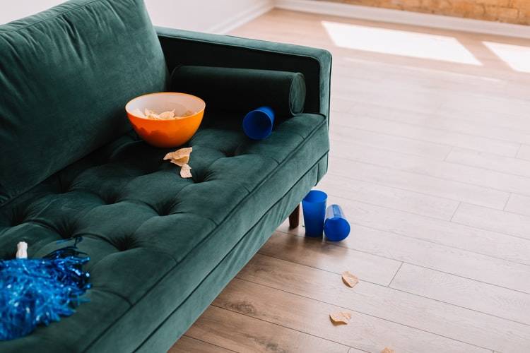Bowl of chips and blue cups scattered on green couch and floor underneath