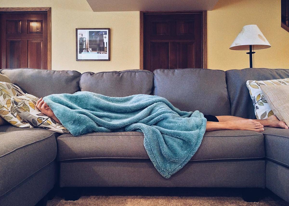 Person sleeping on couch under blue blanket