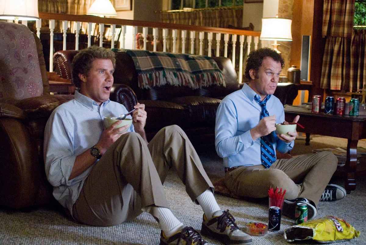 Characters from the movie Step Brothers sitting eating in front of the TV