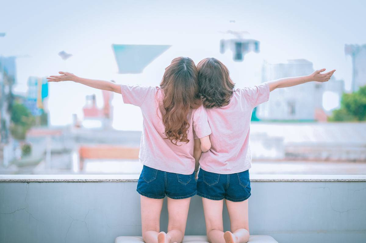 Two girls in matching outfits face away from the camera, arms outstretched 