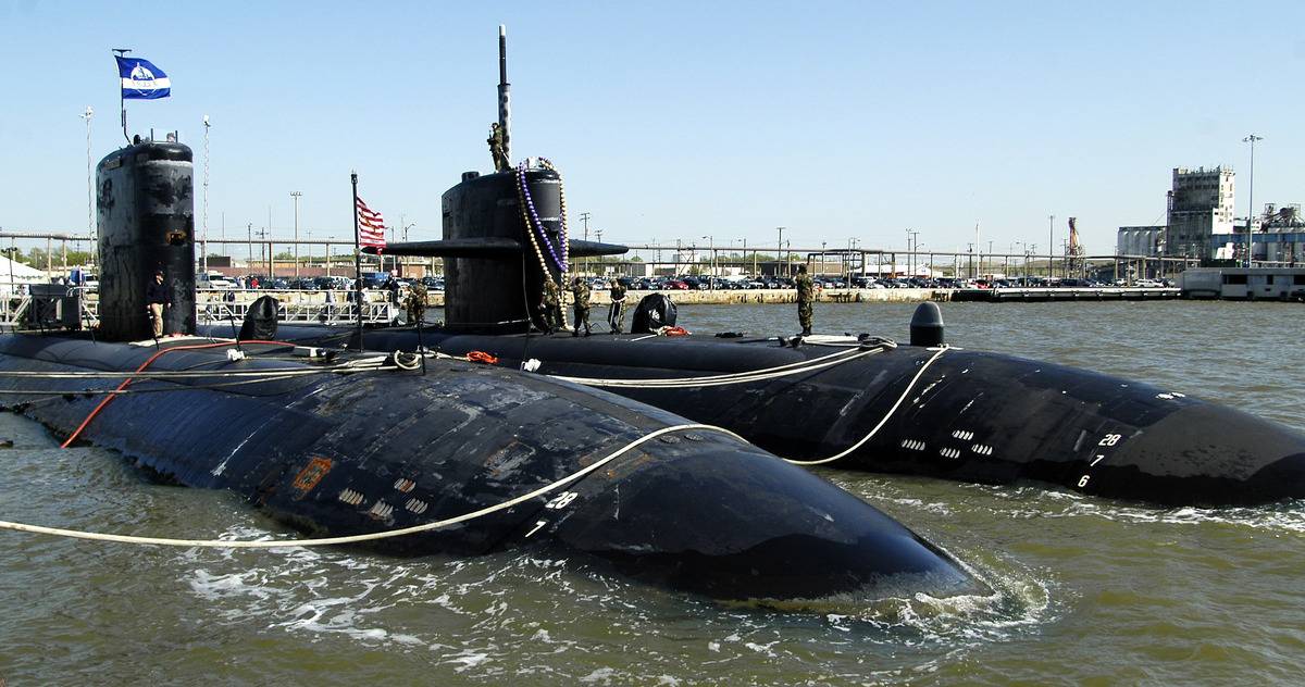 A Virginia-class submarine approaches a shipyard.