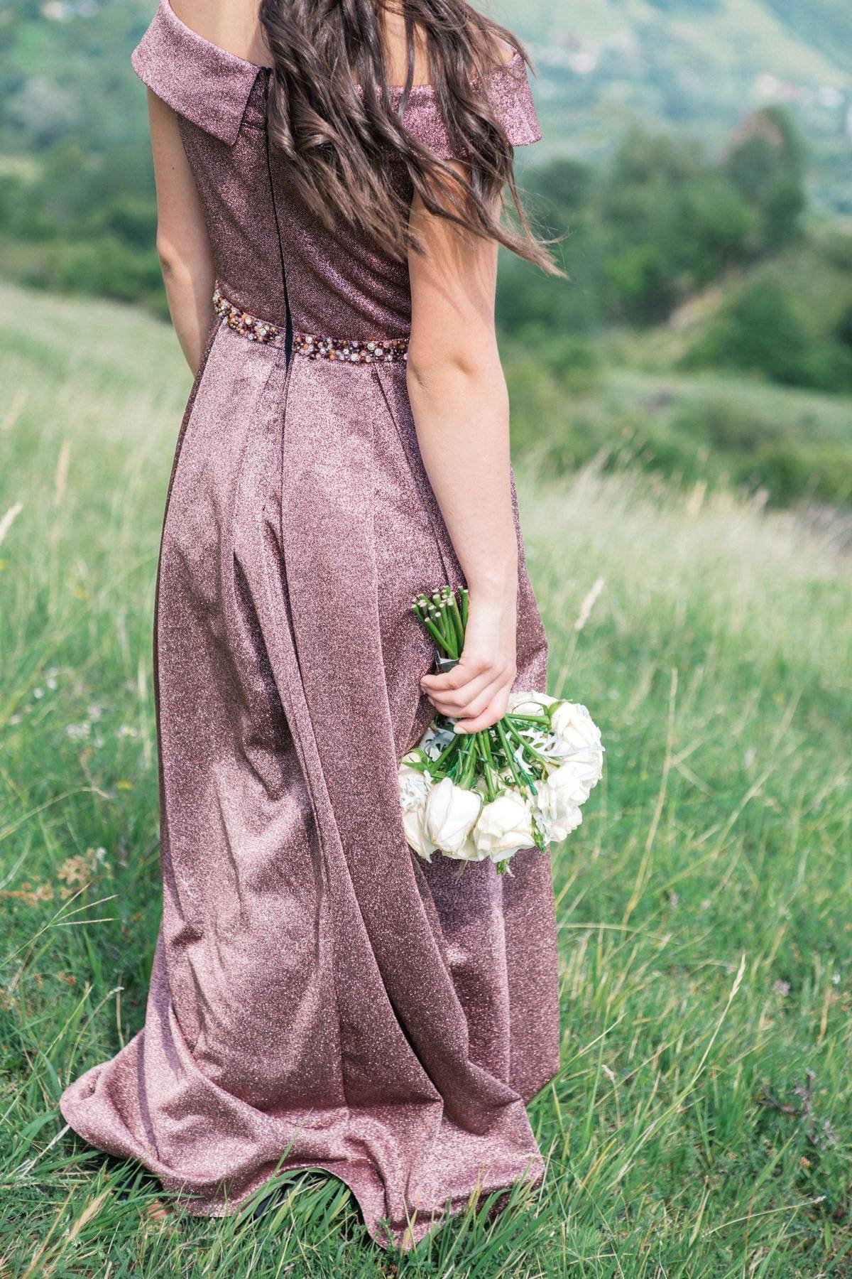 Woman wearing floor-length dress and holding a bouquet standing in a green field
