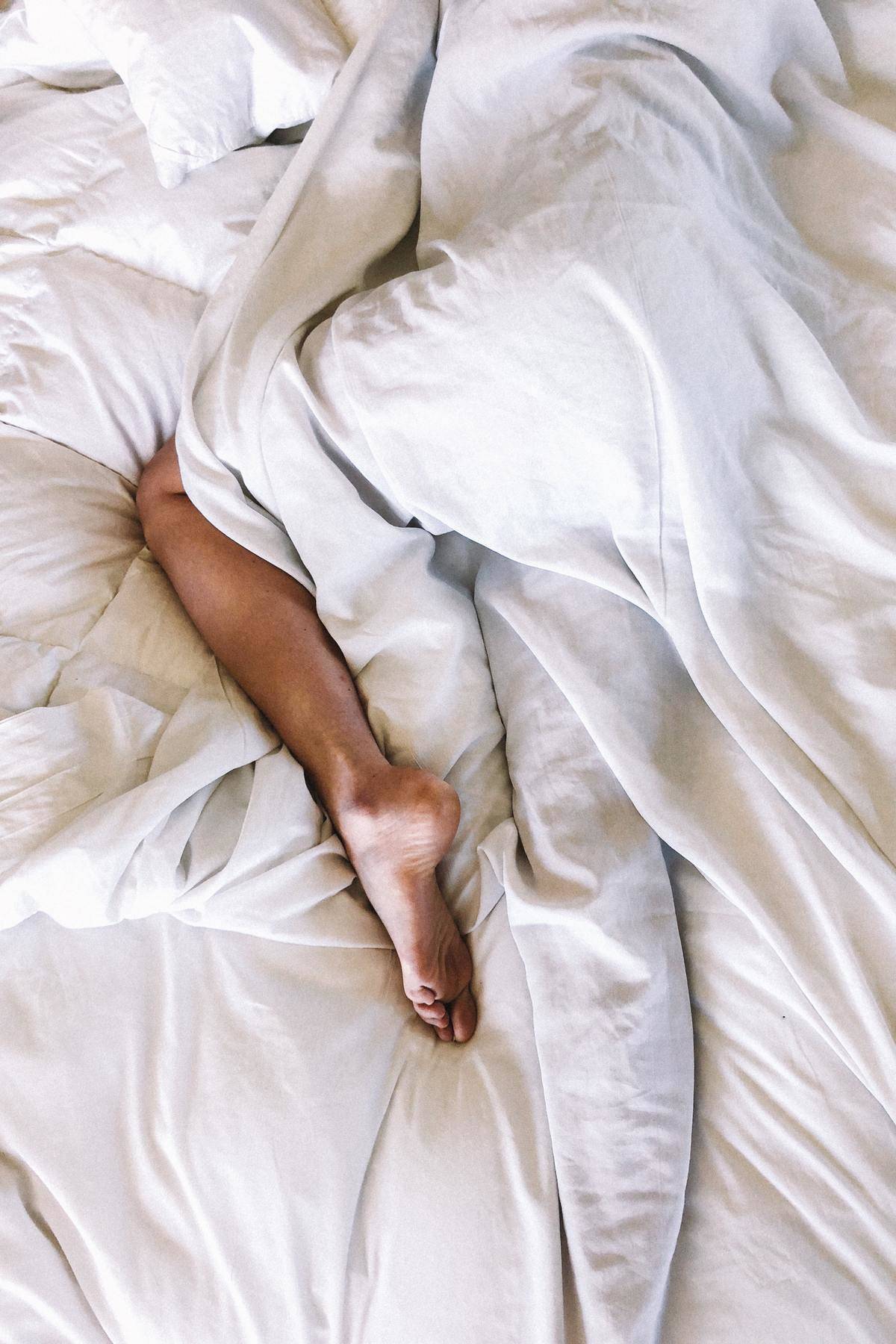 Woman's legs wrapped in white sheet in bed
