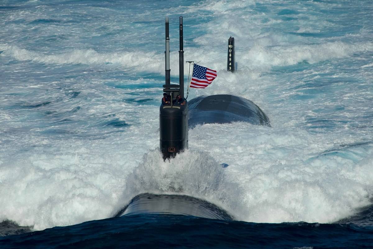 A Navy submarine with an American flag on top coasts across the ocean.