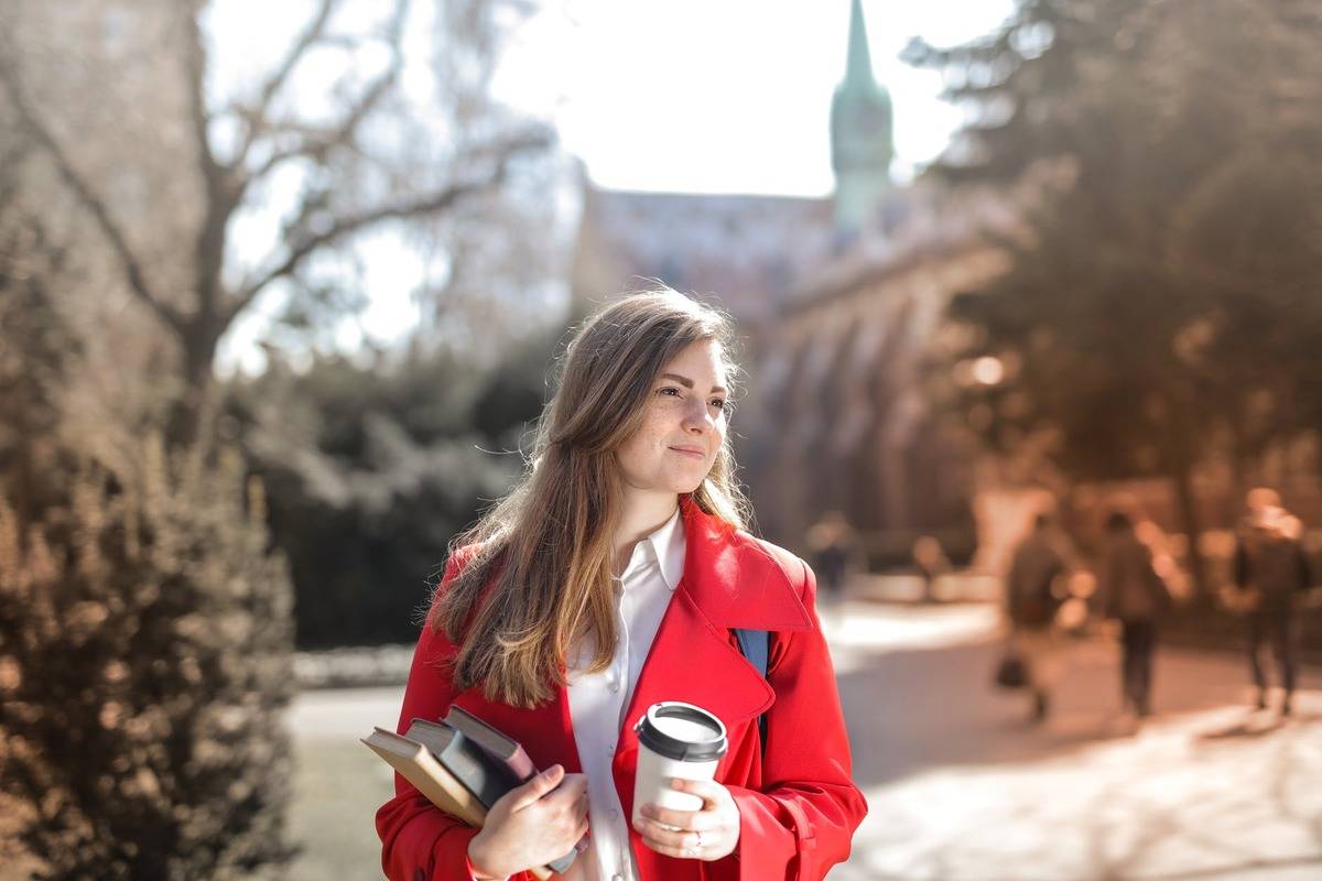 woman smiling holding books and coffee outside on college campus