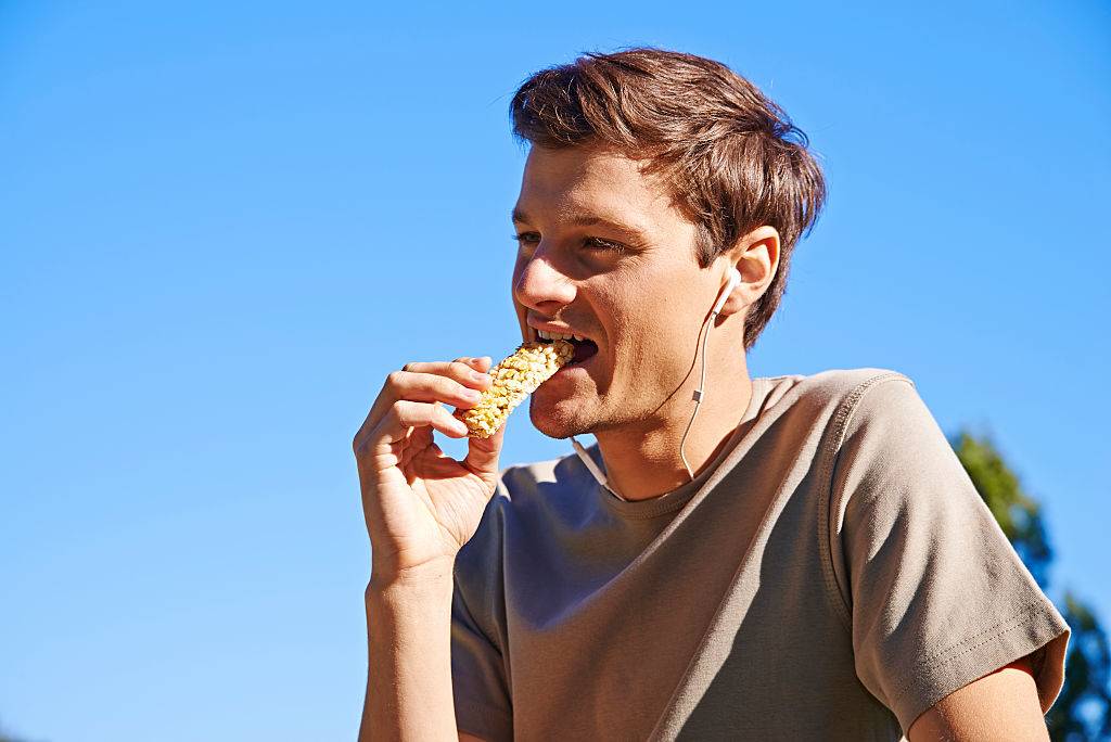 young man eating a granola bar while wearing earbuds