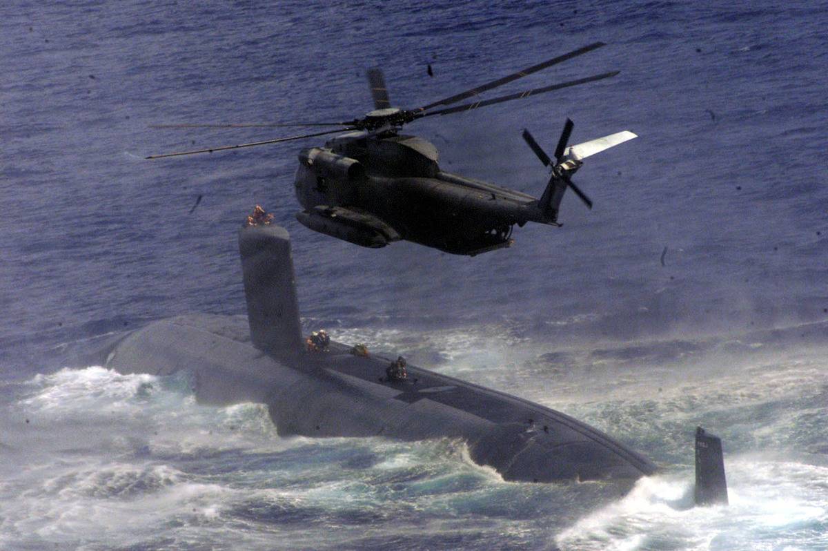 Navy Seals drop from a helicopter onto a submarine during joint training.