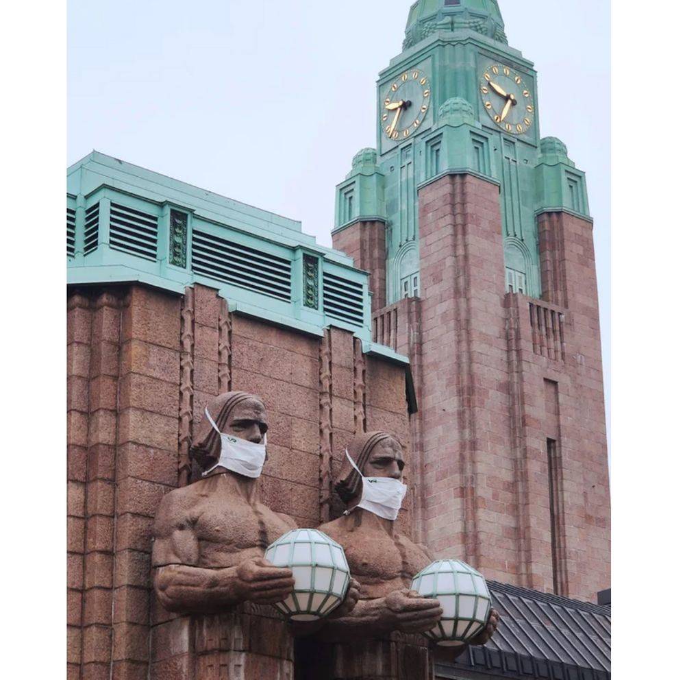 Statues on a building have masks attached to them, worn under their noses