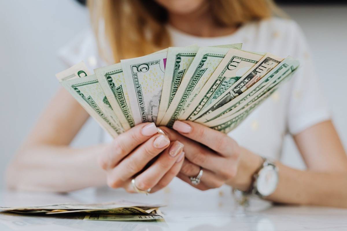 Woman holding $5, $10, and $20 bills fanned out in front of her
