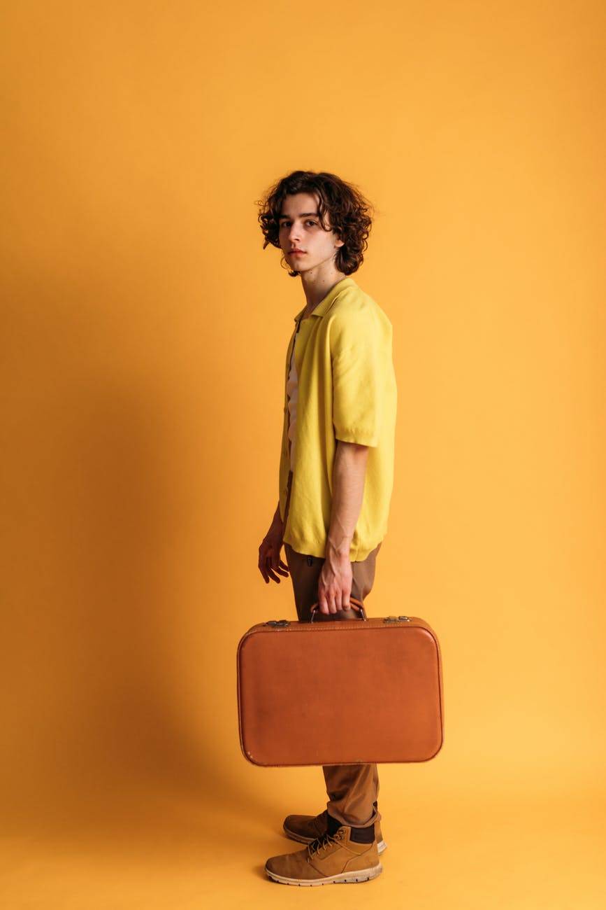 young man holding suitcase against yellow wall