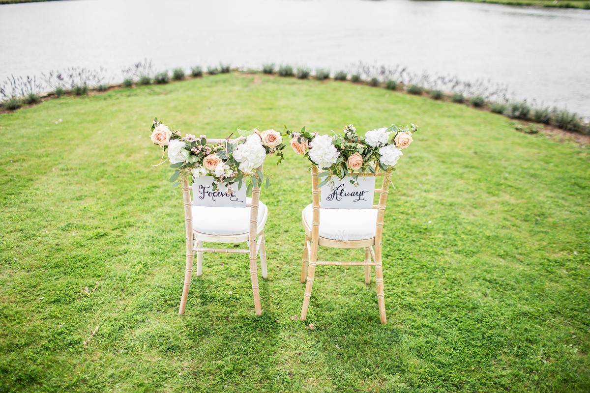 two wedding chairs on the grass by the water