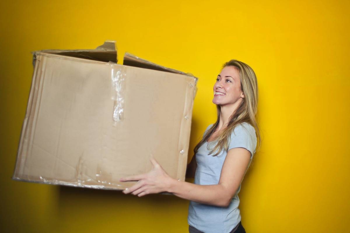 woman holding moving box and smiling against yellow wall