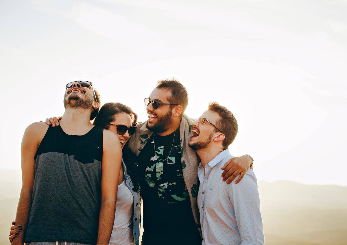 Group of male and female millennials hug and laugh outside 