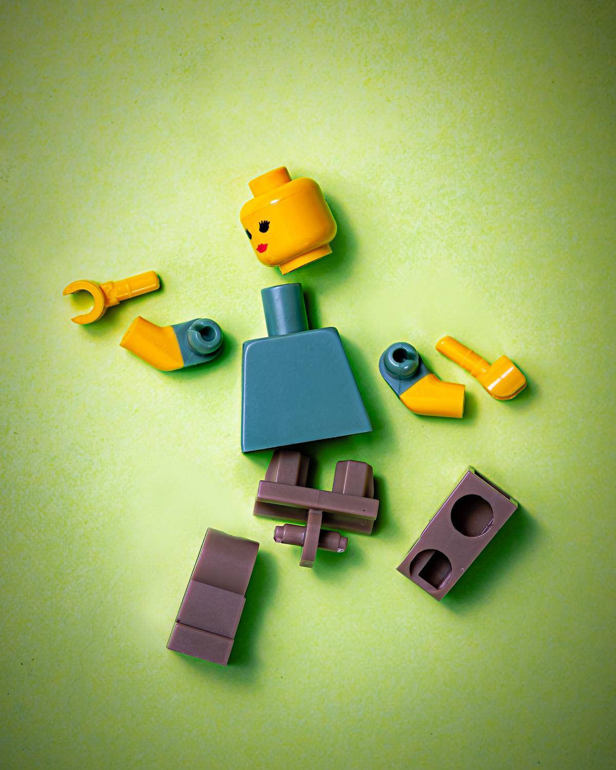 Lego person whose body parts have broken off against a green background