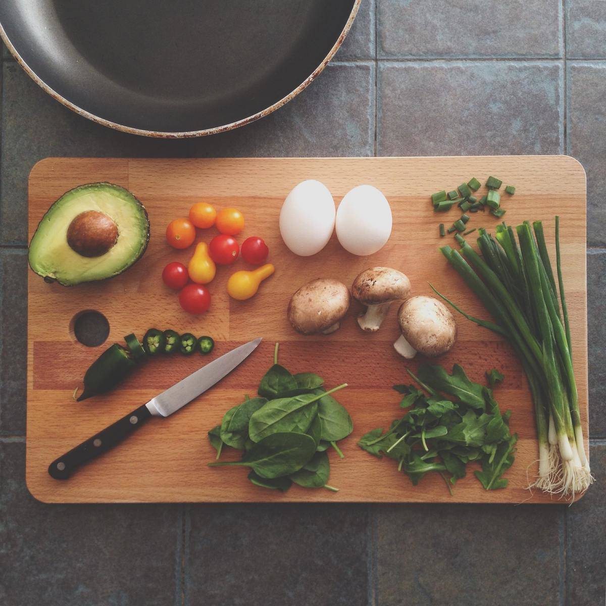 Cutting board with a knife and several ingredients like avocado, eggs, mushrooms and a jalapeno