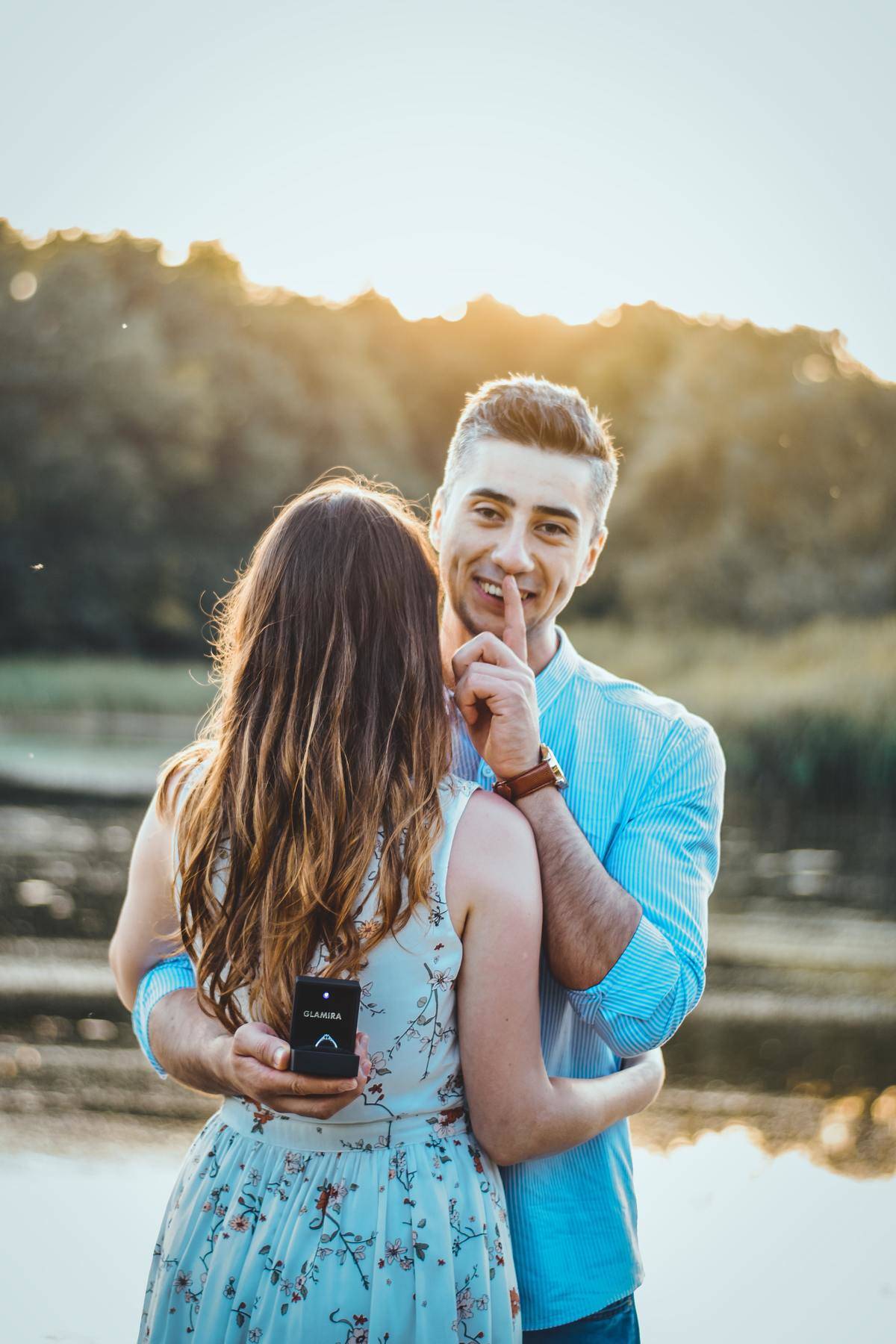 Man with hands to lips shushing with engagement ring hidden behind woman's back