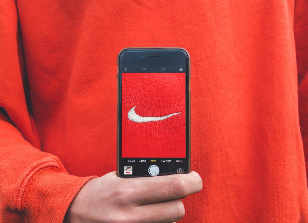 A man holds an iPhone whose camera is pointed at the Nike logo on his shirt 