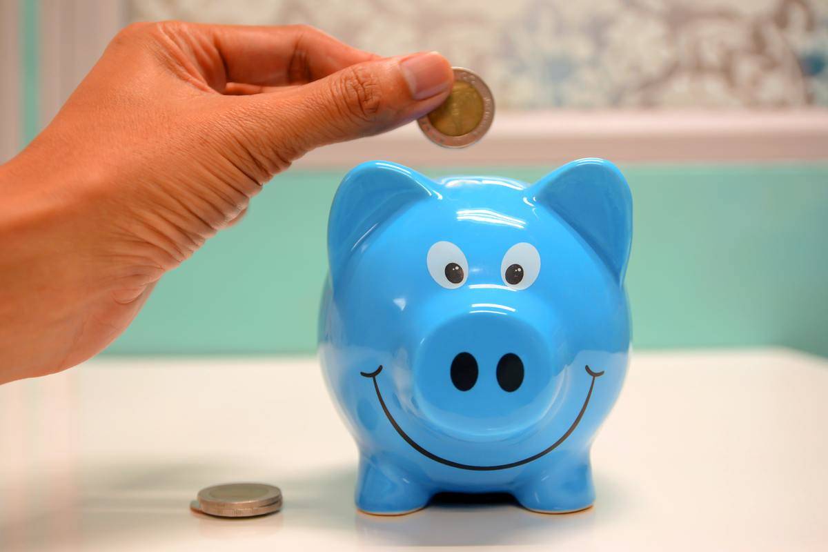 Person puts a coin inside a blue piggy bank