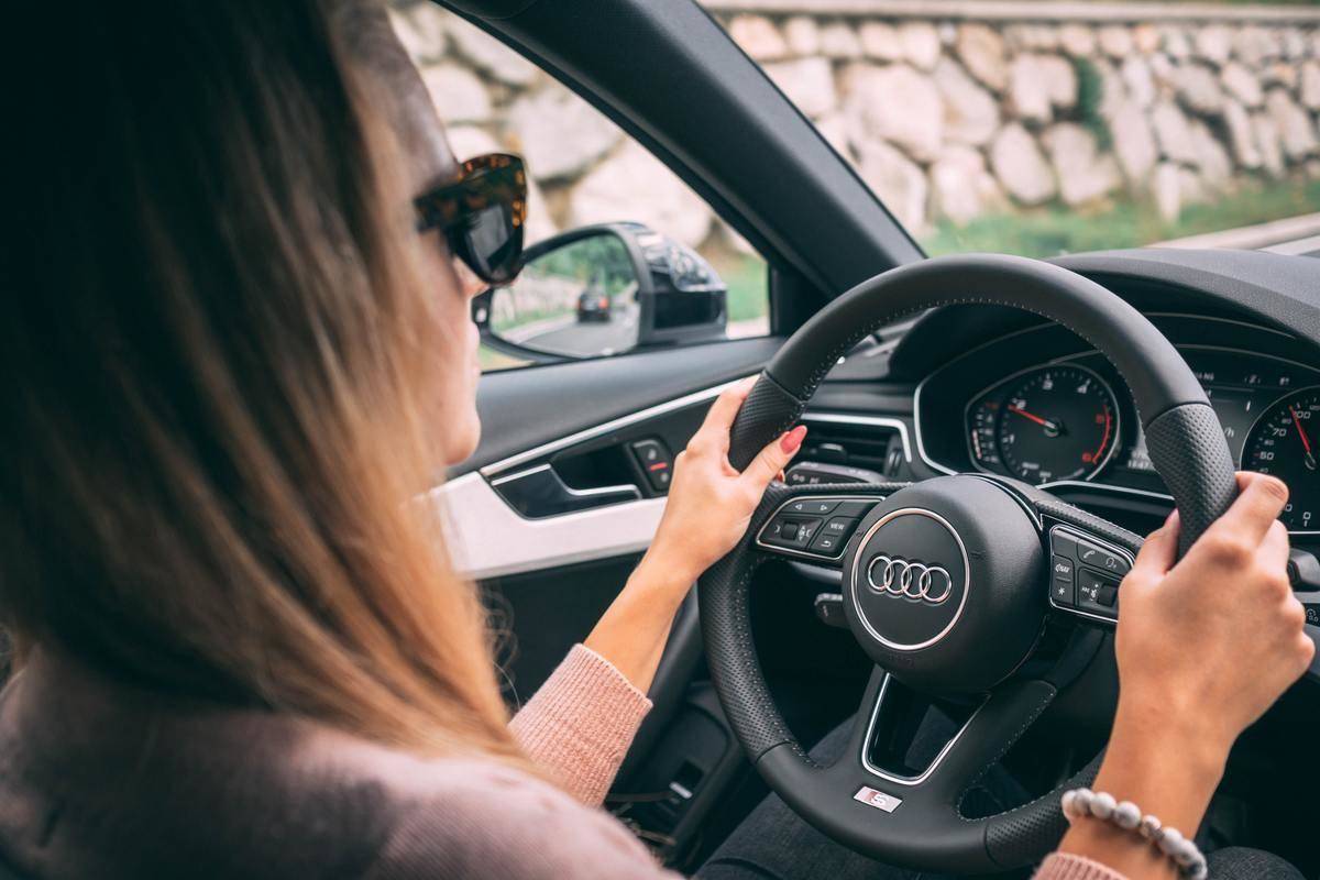 Audi steering wheel with woman's hands holding wheel, pearl bracelet and red nails.