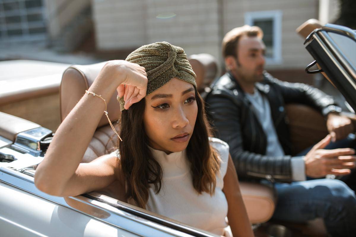 Couple in convertible with woman resting her arm against the window looking upset