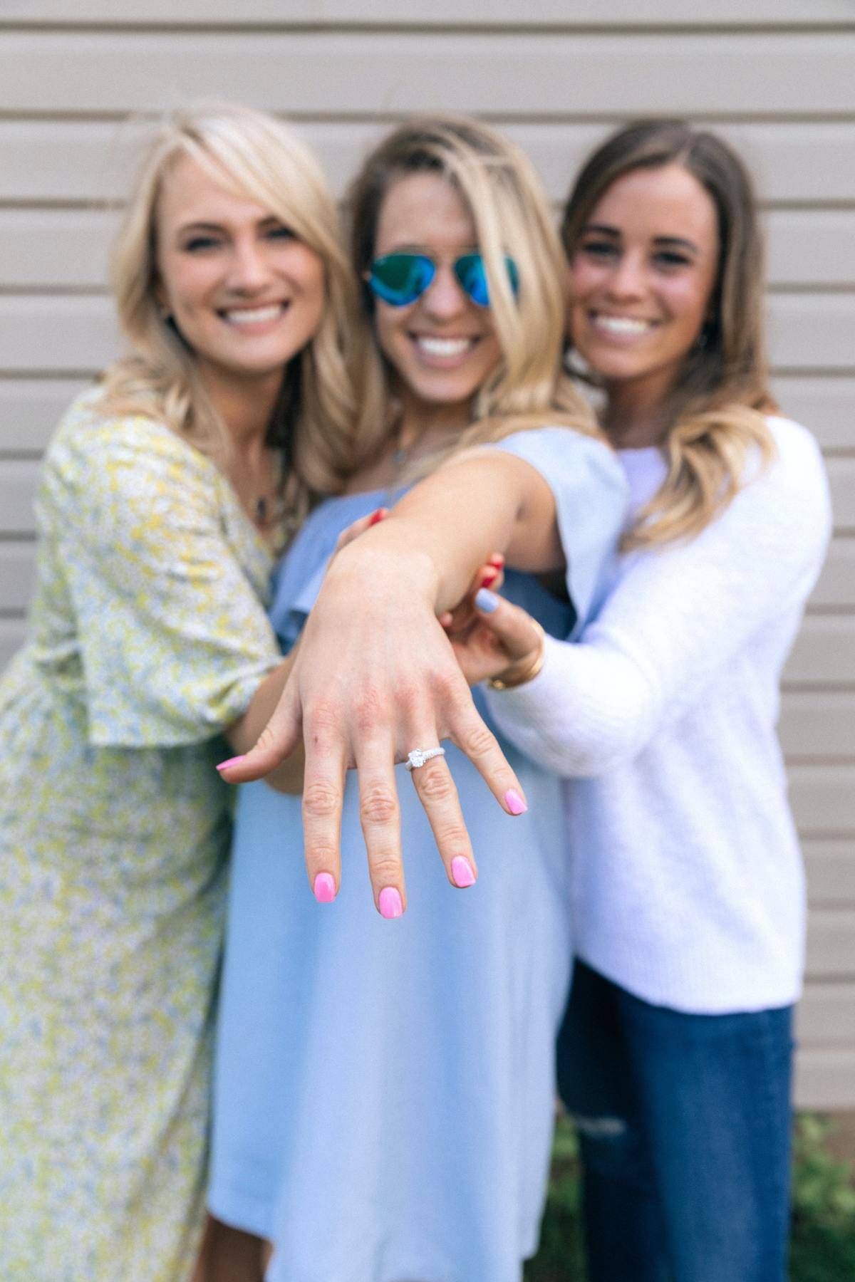 Woman showing off engagement ring smiling with two friends