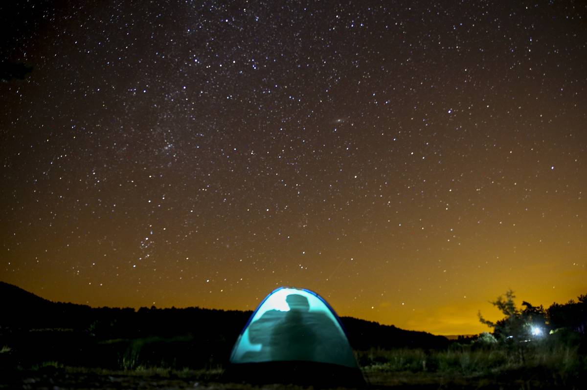 People camp in a tent underneath a starry sky.
