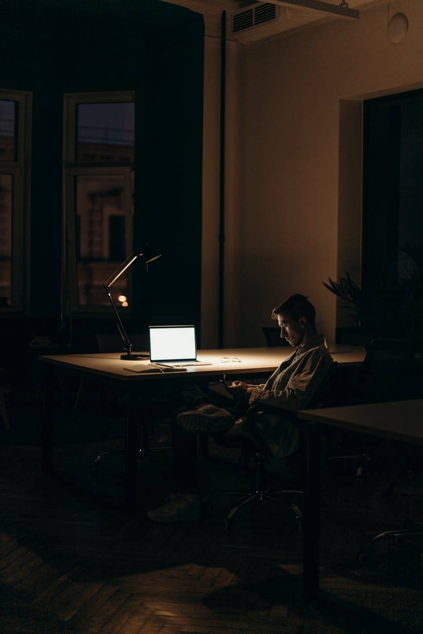 man on laptop and phone in dark room