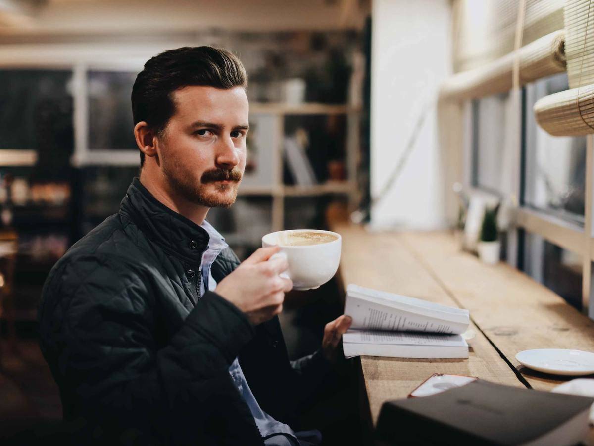 a man drinking a cup of coffee and reading a book