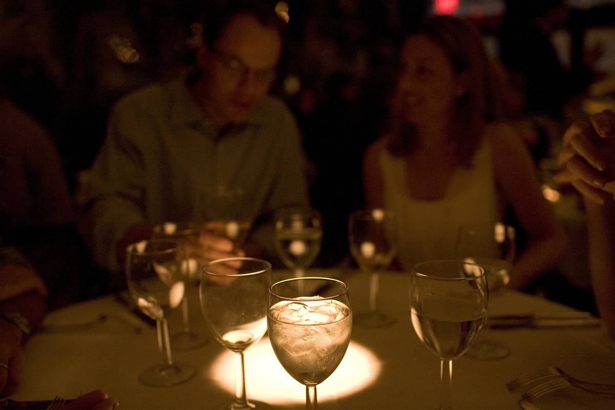 Water and wine glasses are highlighted in a dimly-lit restaurant.