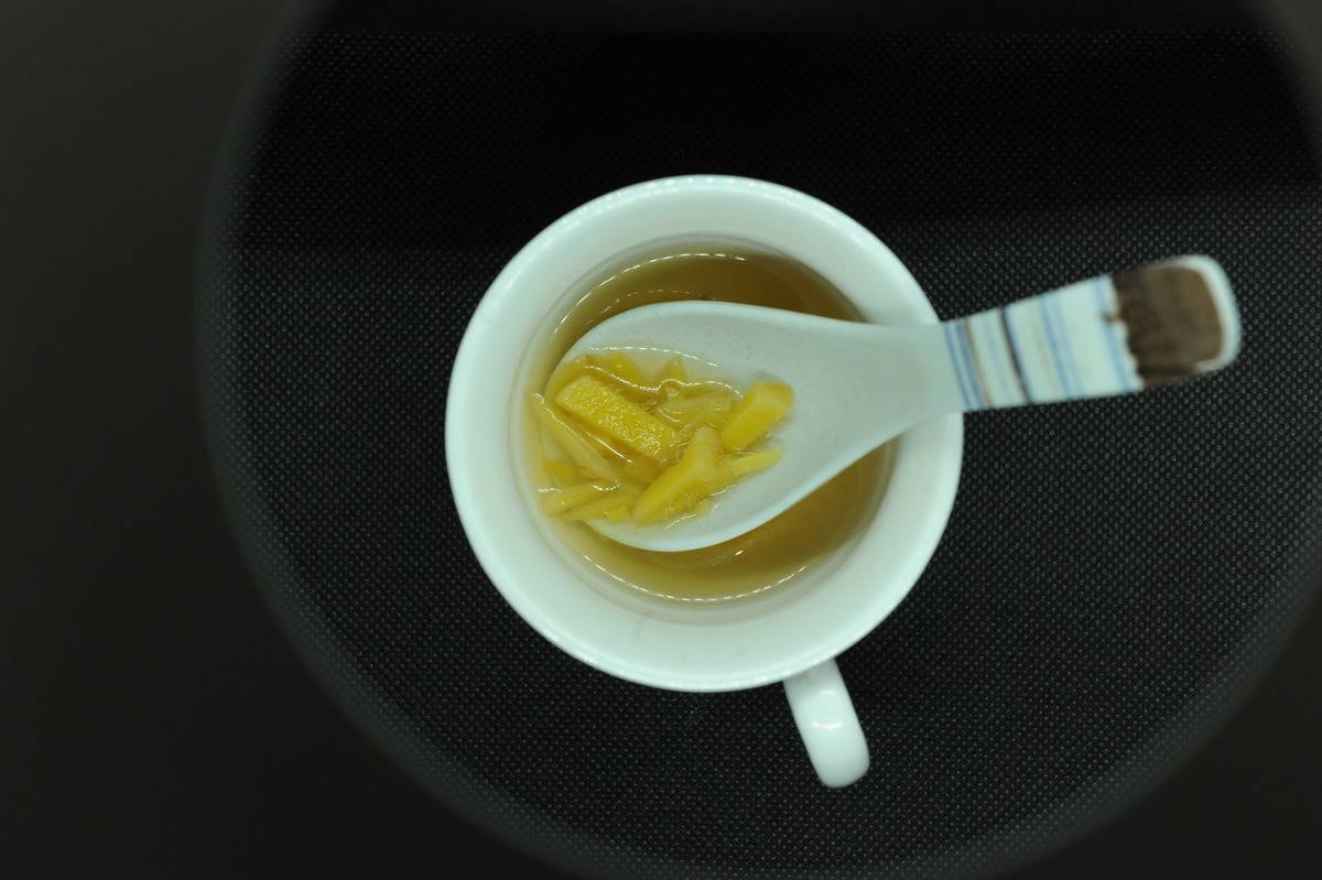 A spoon digs out chopped ginger from a cup of tea.