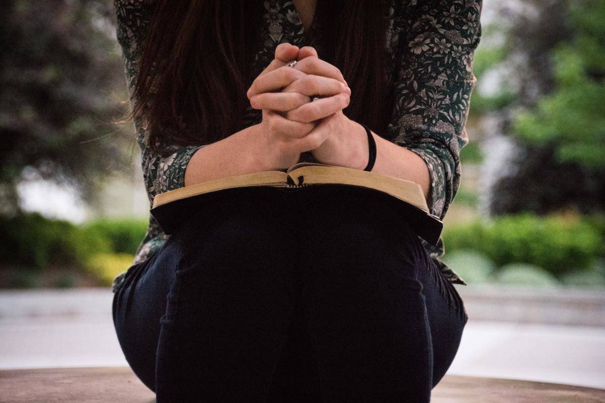 a woman clasping her hands with a book on her lap