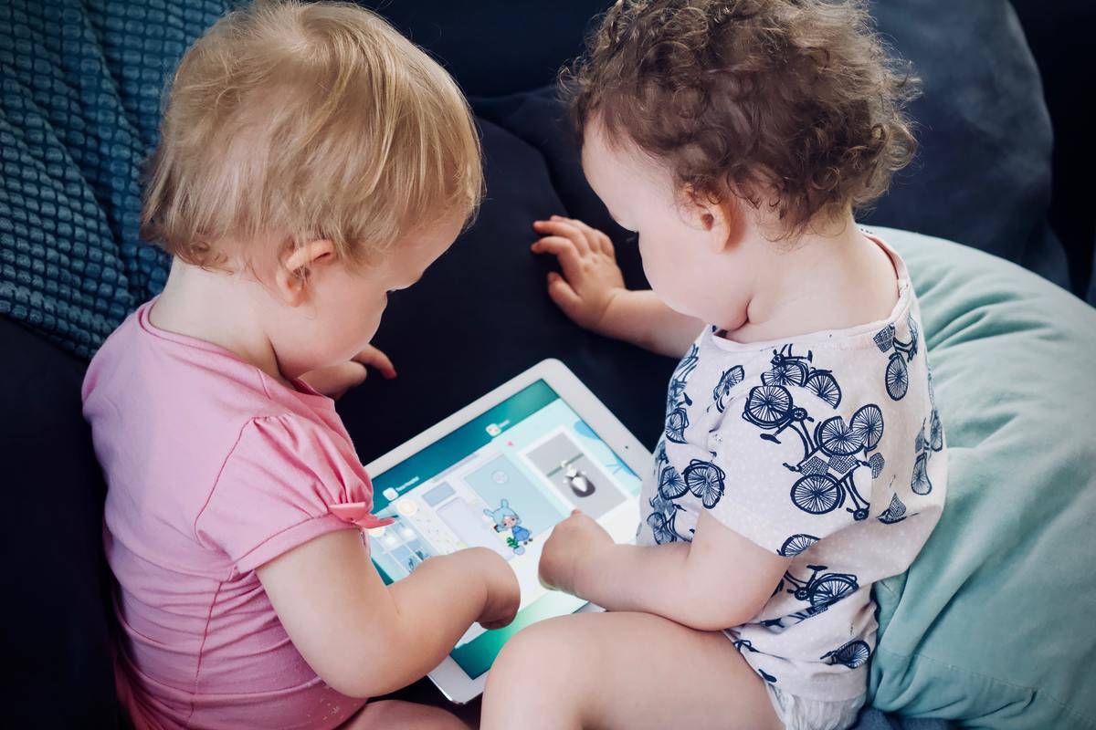 Two baby girls look away from the camera and play with an iPad
