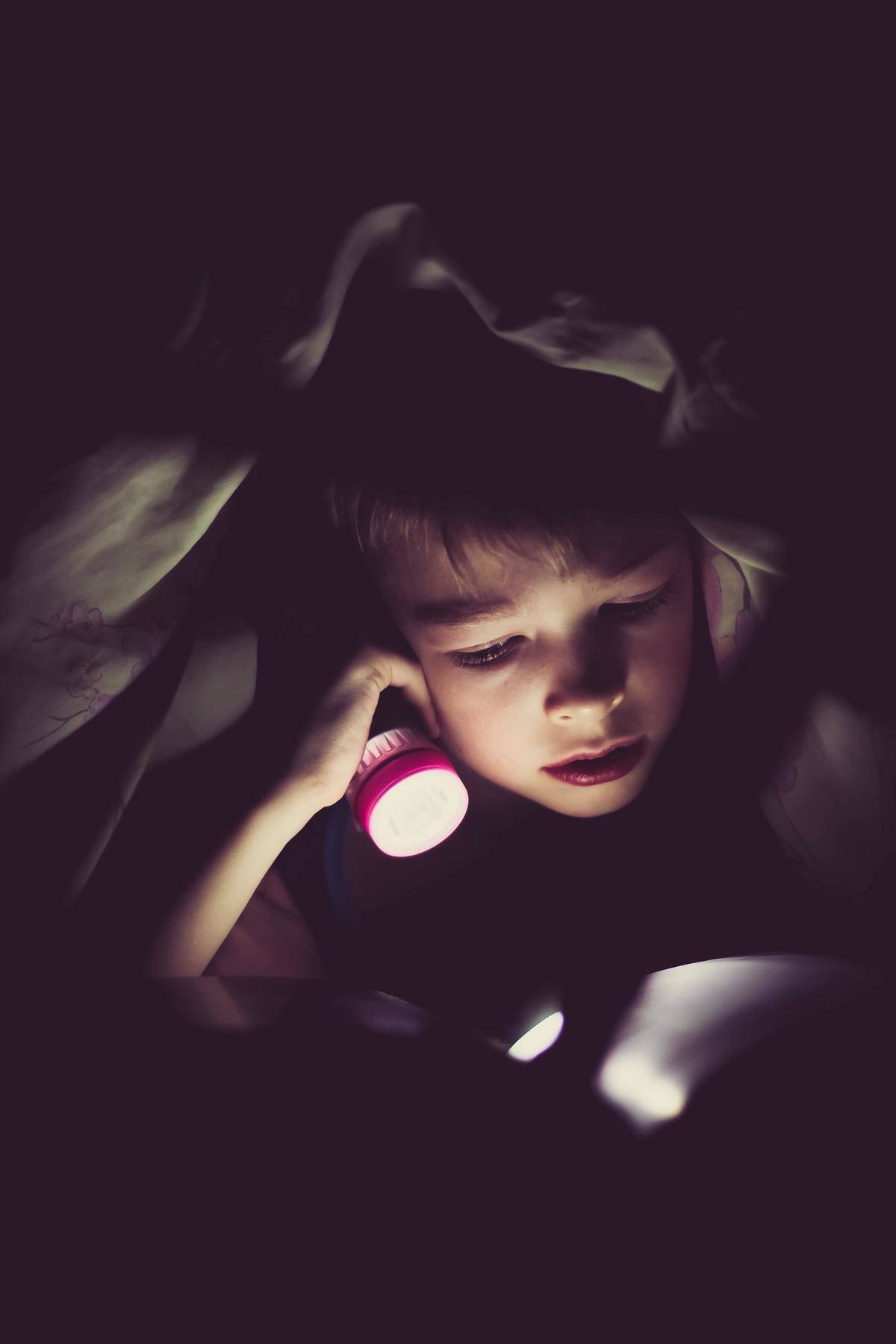 kid reading under covers